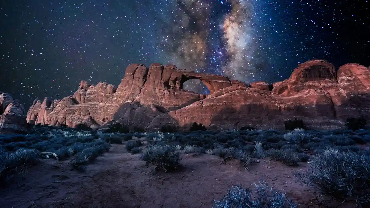 A dark blue sky with a subtle glow of starlight forms a celestial window above Skyline Arch, one of Arches National Park's…
