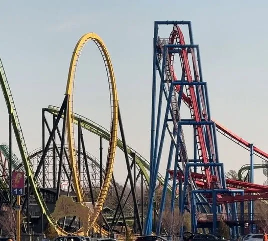 A photo of multiple colorful roller coasters at an amusement park, including a prominent yellow loop and a red track with a…