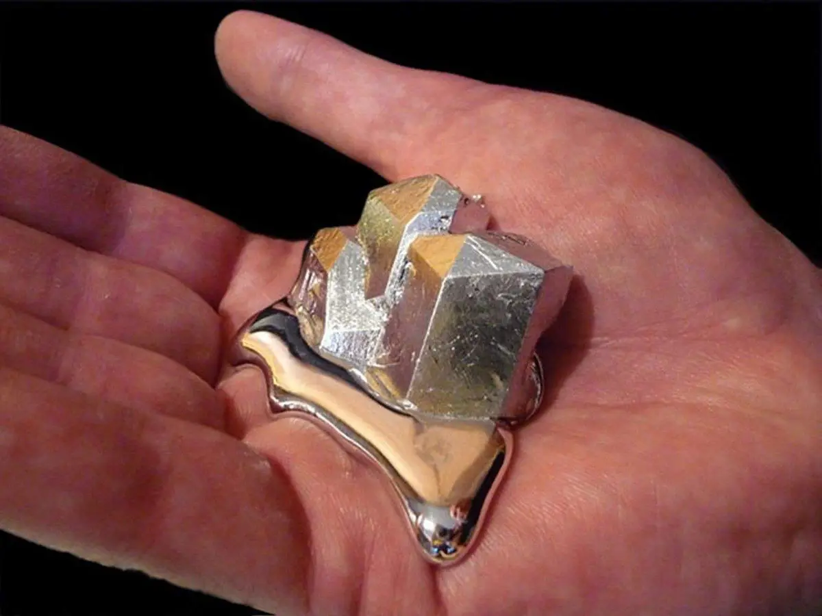 A hand holds a metallic object that appears to be melting or dripping, with a crystalline, geometric top portion and a…