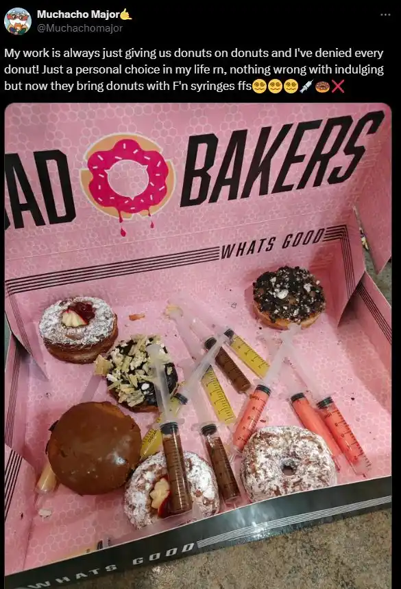 A pink box from 'BAD BAKERS' contains several donuts with syringes inserted into them, filled with various colored liquids…