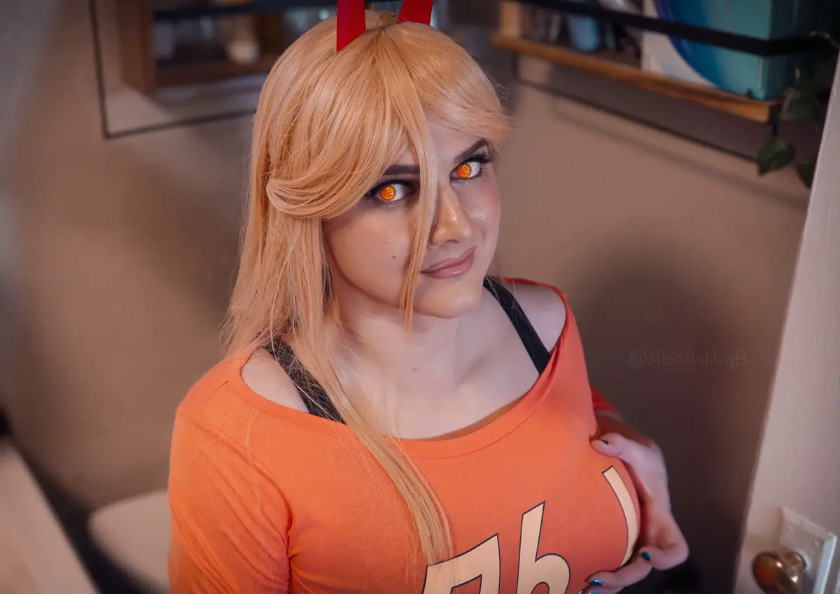 A person in a cosplay of the anime character Hellsing's Alucard, wearing an orange shirt, red horns, and glowing orange…