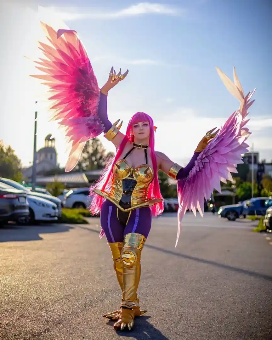 A person in a detailed cosplay of a fantasy character with large, elaborate pink and purple feathered wings stands in a…