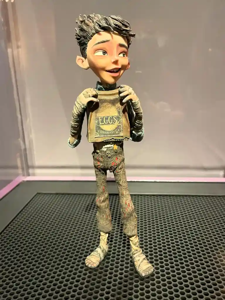 A detailed figurine of a young animated character with messy dark hair, wearing tattered clothes and holding up a weathered…