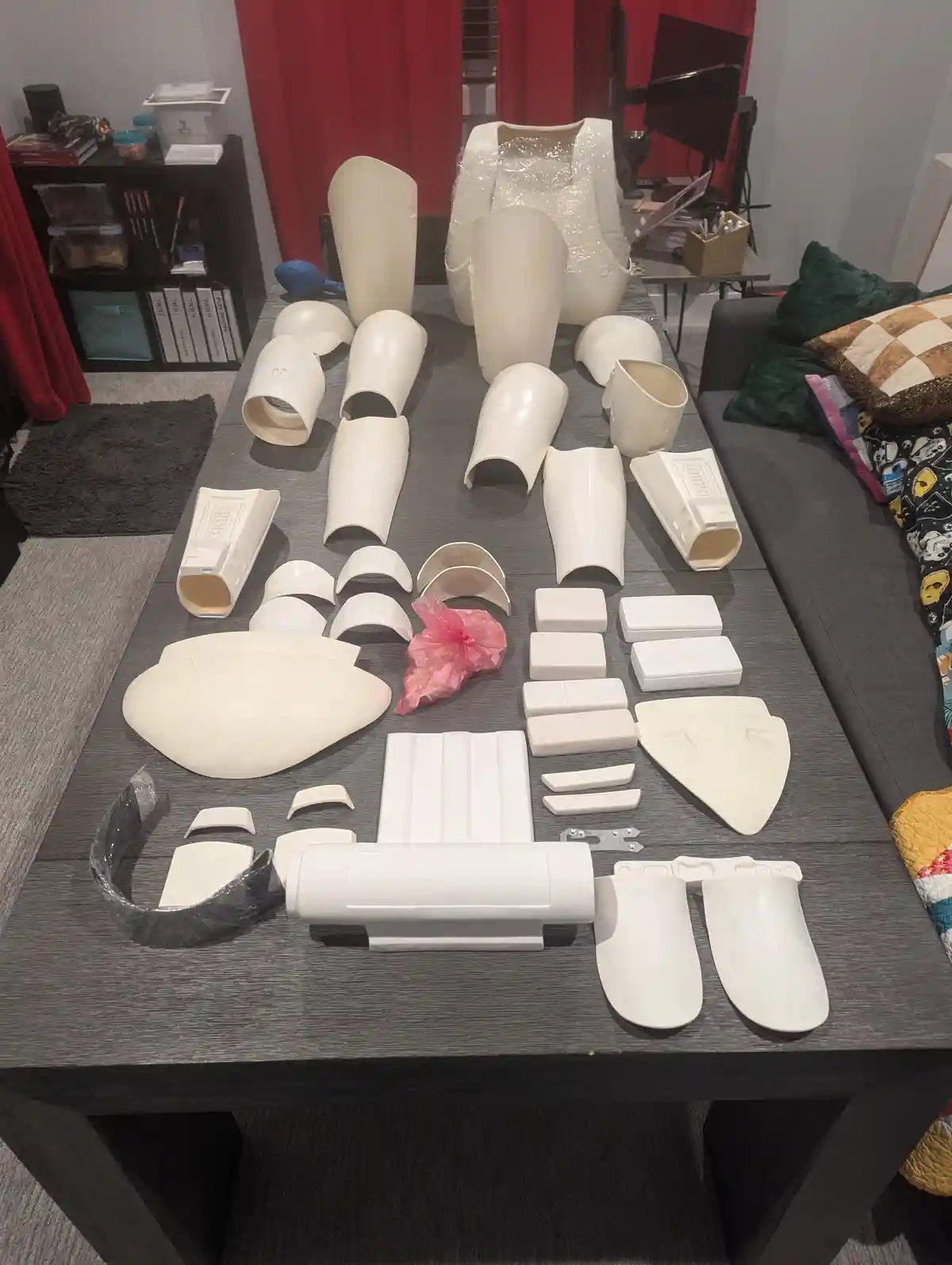 A dark gray table is covered with numerous white plastic costume pieces, including arm, leg, and torso segments, some still…