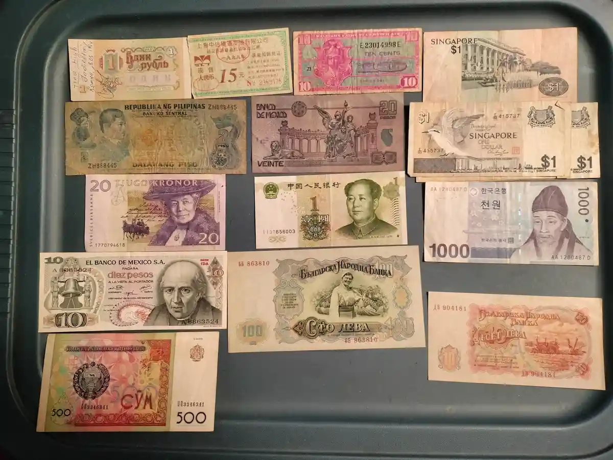 A dark gray plastic tray holds a collection of various old and foreign banknotes, including Soviet rubles, Philippine pesos…