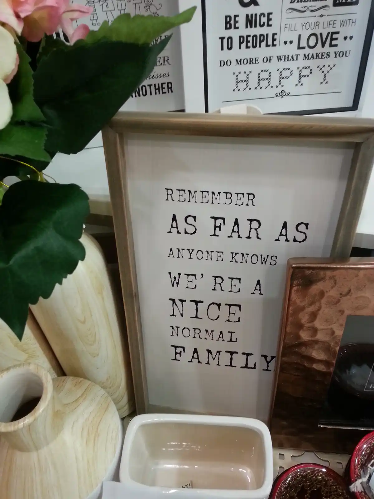 A framed sign with black text on a light background reads 'REMEMBER AS FAR AS ANYONE KNOWS WE'RE A NICE NORMAL FAMILY'…