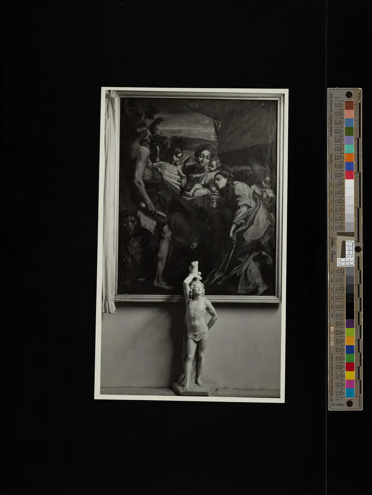 A black-and-white photograph shows a classical marble statue of a nude youth holding a torch aloft, standing on a ledge…