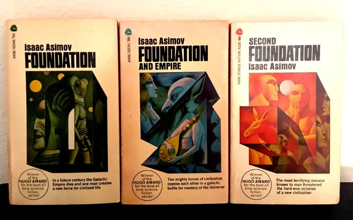 Three vintage paperback books by Isaac Asimov are displayed side-by-side, titled 'Foundation', 'Foundation and Empire', and…