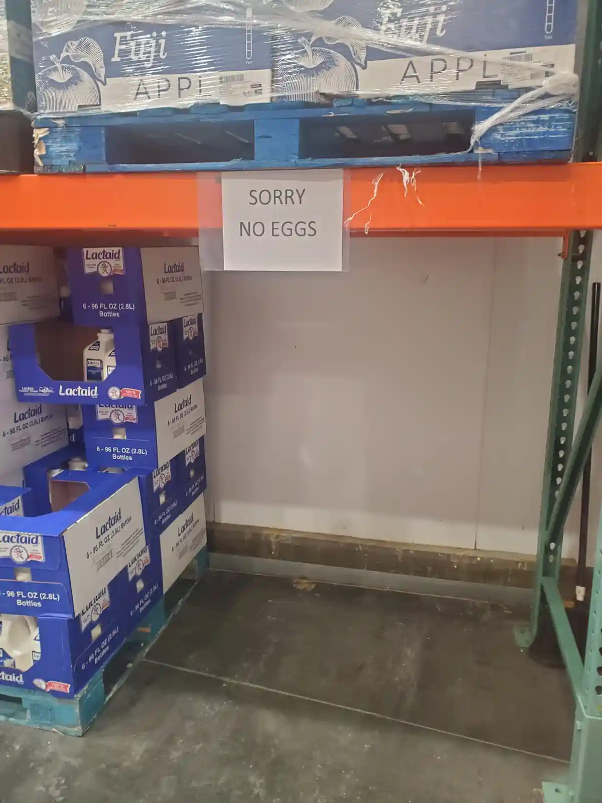 A photo of a warehouse shelf with boxes of Lactaid lactase enzyme supplements and Fuji apples on pallets, with a handwritten…