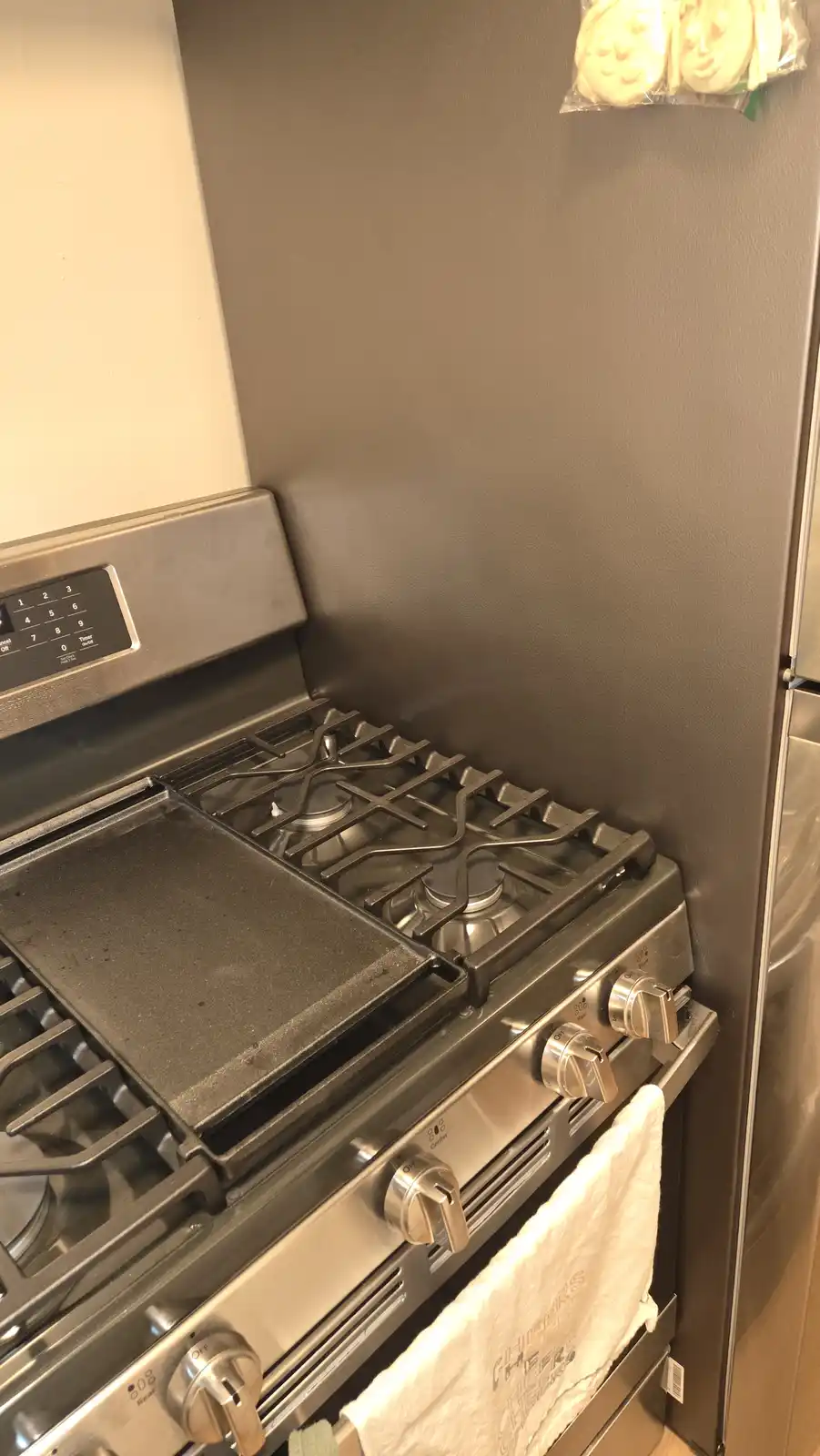 A stainless steel gas stove with a griddle and burners sits next to a refrigerator, with a white towel hanging on the oven…