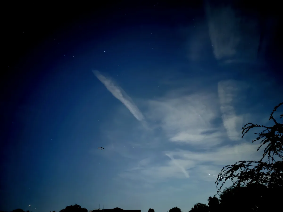 A night sky with stars and wispy clouds, featuring a black arrow pointing to a thin, elongated cloud formation. The…