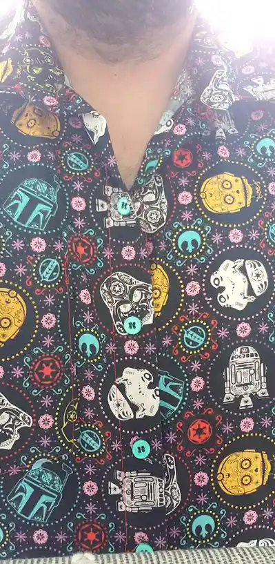 A close-up of a person's chest wearing a black button-up shirt with a colorful pattern of Star Wars characters like Boba…