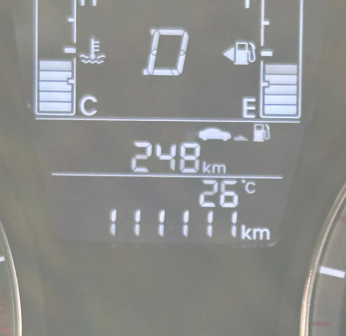 A close-up of a car's digital dashboard showing 248 km driven, 26°C temperature, and a fuel gauge indicating low fuel with a…