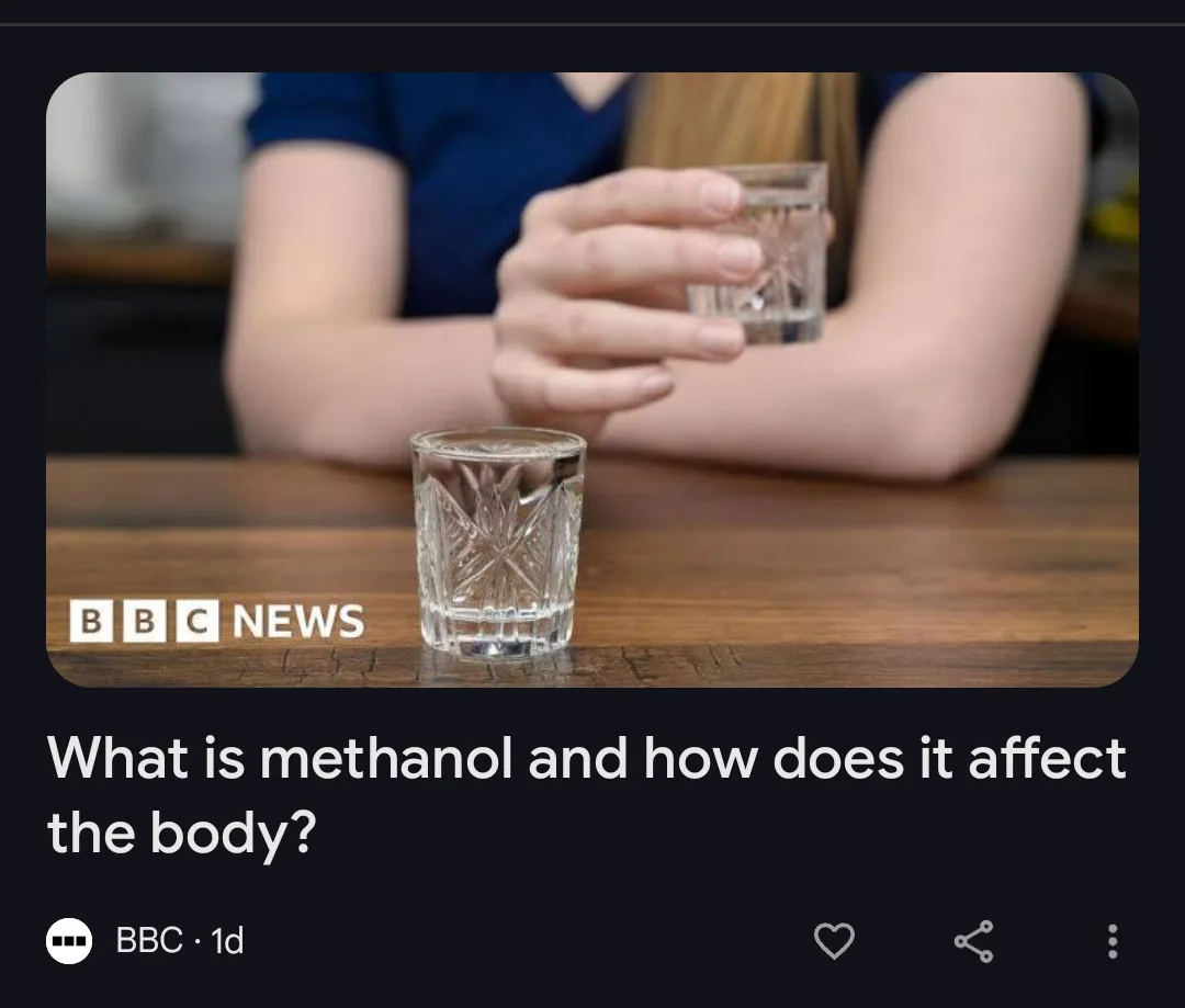 A person in a blue shirt holds a glass of clear liquid while another identical glass sits on a wooden table. The image is…