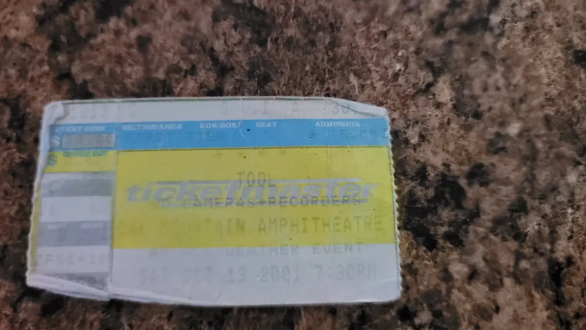 A close-up of a worn Ticketmaster concert ticket for the band Tool, dated September 13, 2001, lying on a speckled…