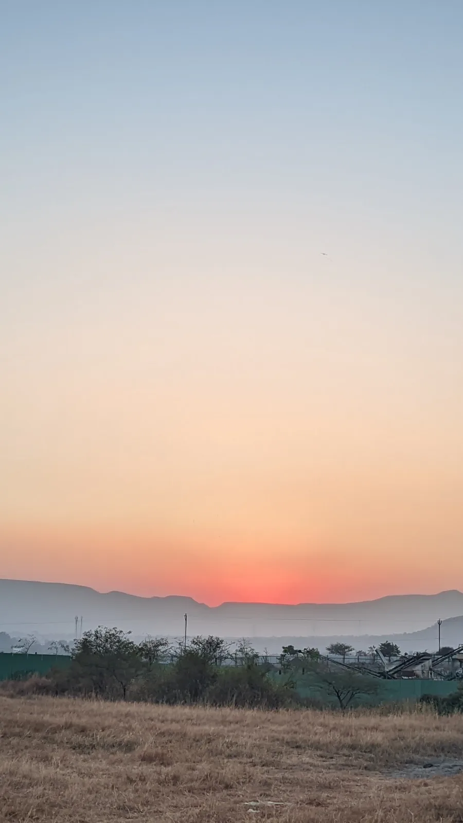A serene landscape photo of a sunset over distant mountains with dry grass in the foreground and sparse trees, overlaid with…