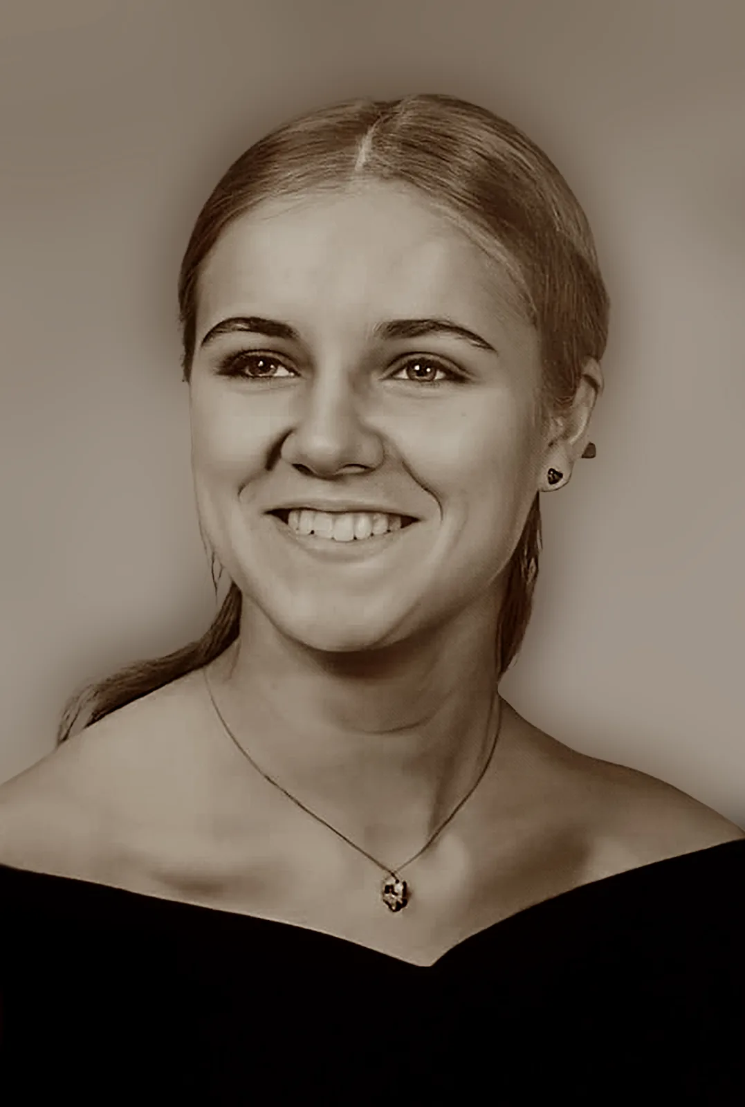 A sepia-toned portrait of a smiling young woman with her hair pulled back, wearing a black top and a necklace with a…