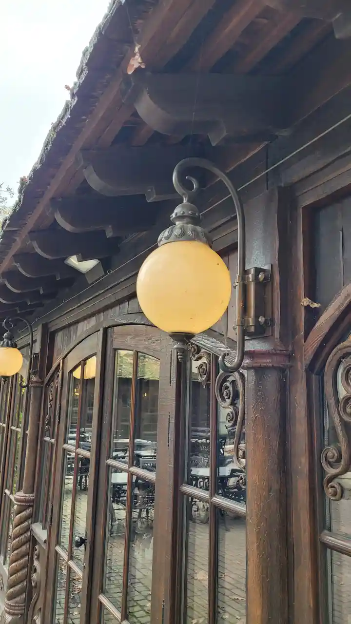 A close-up photo of an ornate, vintage-style outdoor lamp with a frosted glass globe mounted on a dark wooden building…
