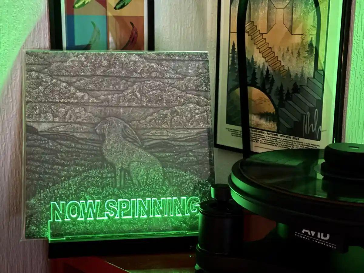 A close-up shot of a vinyl record player with a glowing green 'NOW SPINNING' sign in front of it. The sign features a…