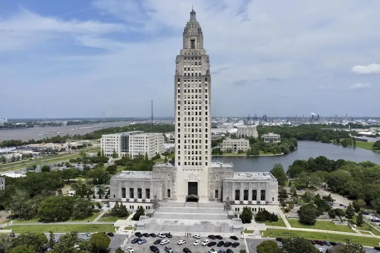 An aerial photo shows the tall, ornate Louisiana State Capitol building surrounded by greenery and parking lots, with a…