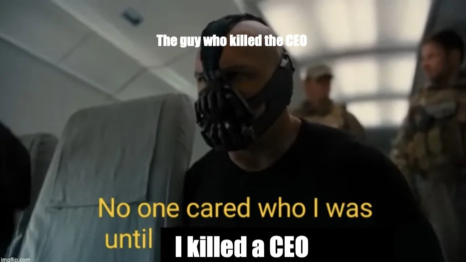 A man wearing a black, mechanical, bat-like mask stands in what appears to be an airplane cabin, with other people in…