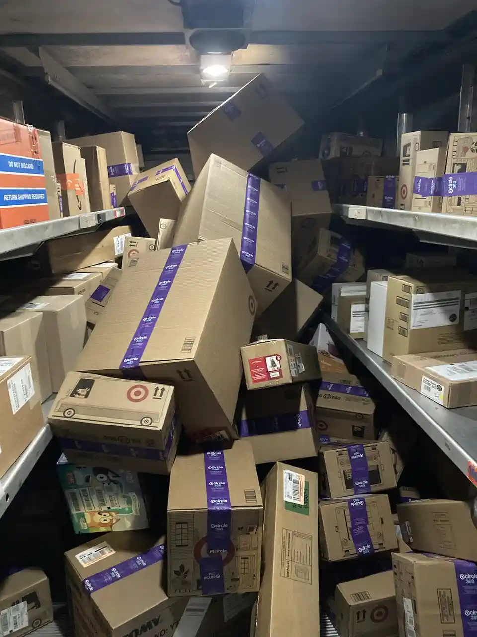 A cluttered warehouse aisle filled with cardboard boxes, many bearing Target's purple 'circle 360' shipping labels and the…