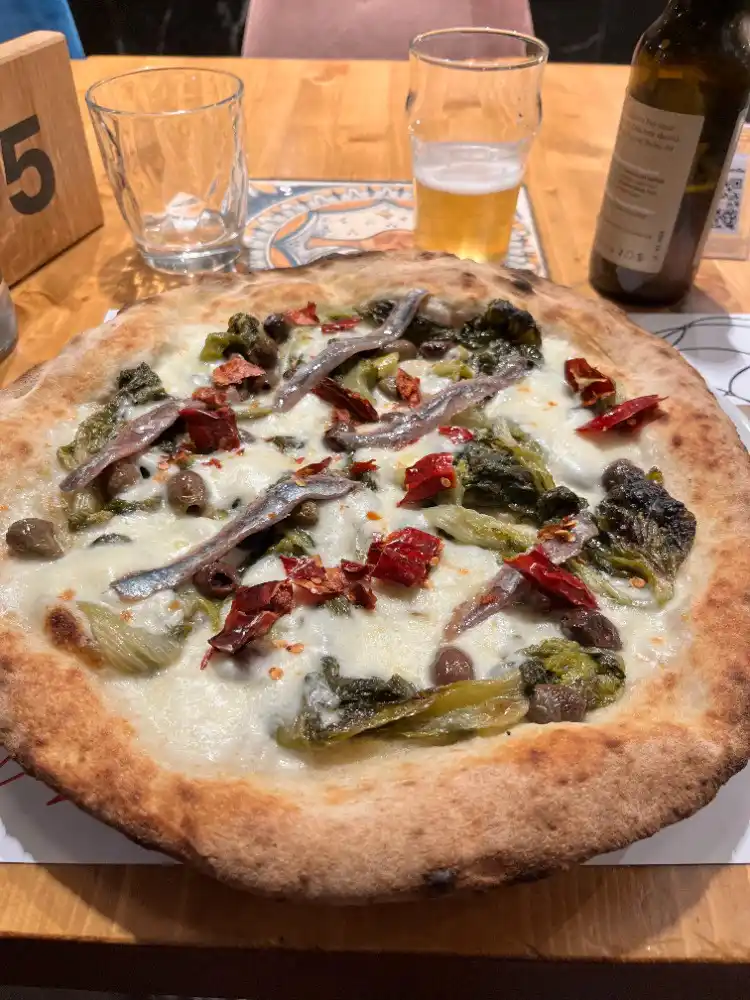 A close-up photo of a rustic pizza with melted cheese, anchovies, olives, and roasted red peppers on a wooden table…