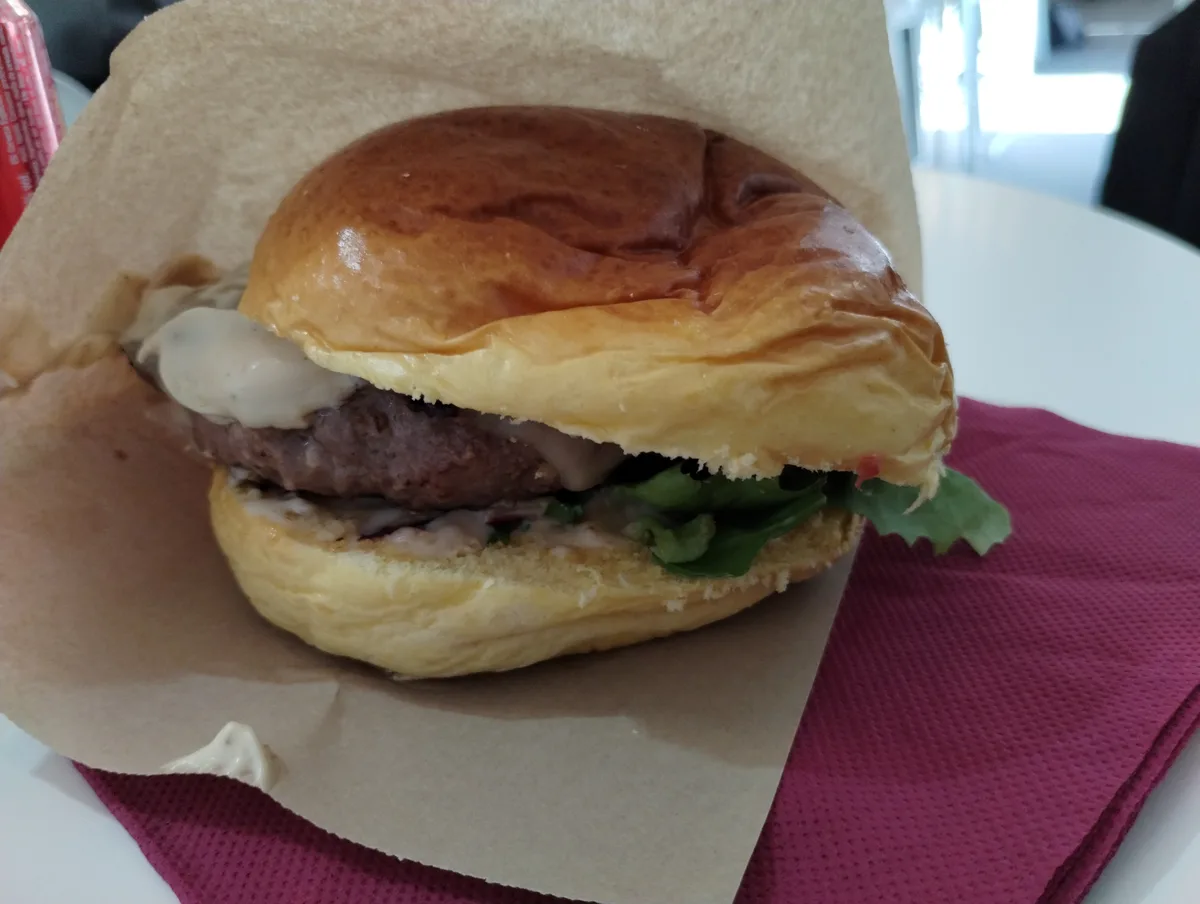 A close-up photo of a juicy burger with a beef patty, melted white sauce, and green lettuce, nestled in a soft bun and…
