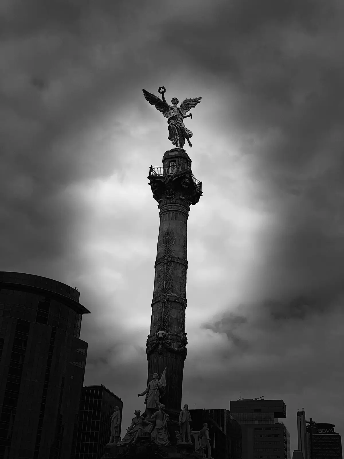 A black-and-white photograph shows the Angel of Independence monument in Mexico City, a tall column topped by a winged angel…