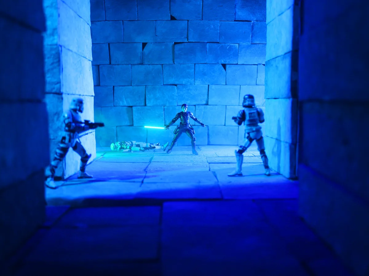 A staged scene with Star Wars action figures: a central figure holding a glowing green lightsaber stands between two…