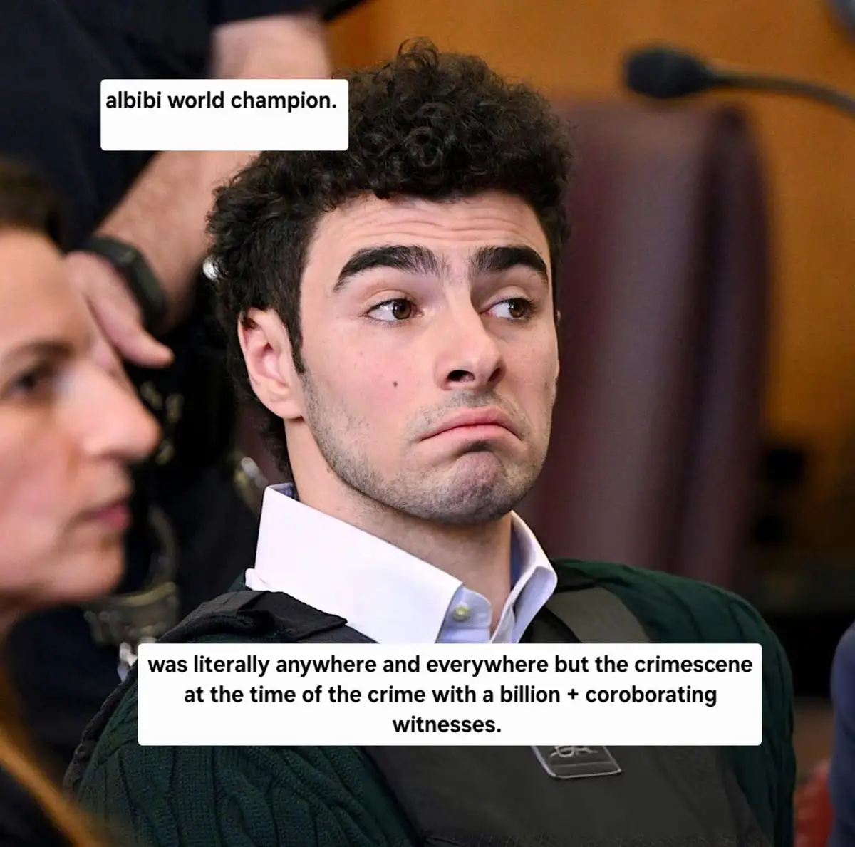 A man with curly dark hair and a skeptical, slightly smug expression is shown in what appears to be a courtroom, wearing a…