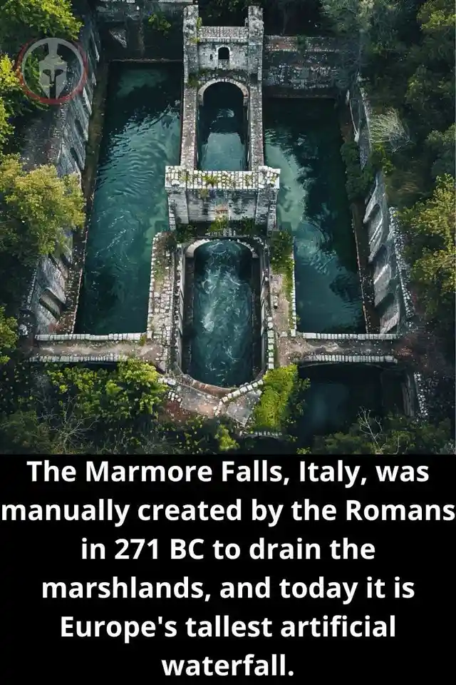 An aerial view shows a large, ancient stone structure with multiple arched channels guiding dark green water through a…
