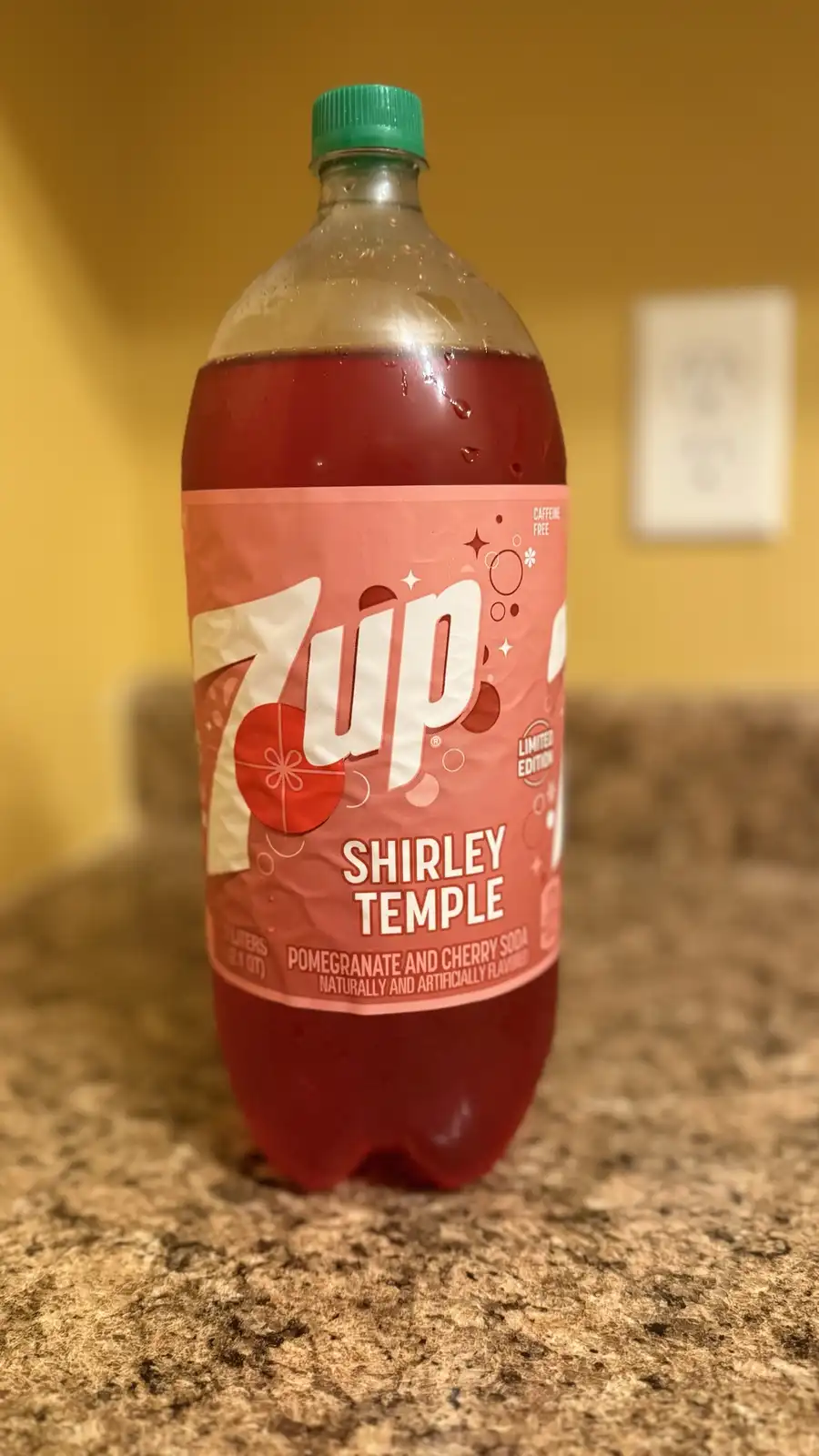 A 2-liter bottle of 7up Shirley Temple soda, with a pink label featuring the brand name and flavor, sits on a speckled…