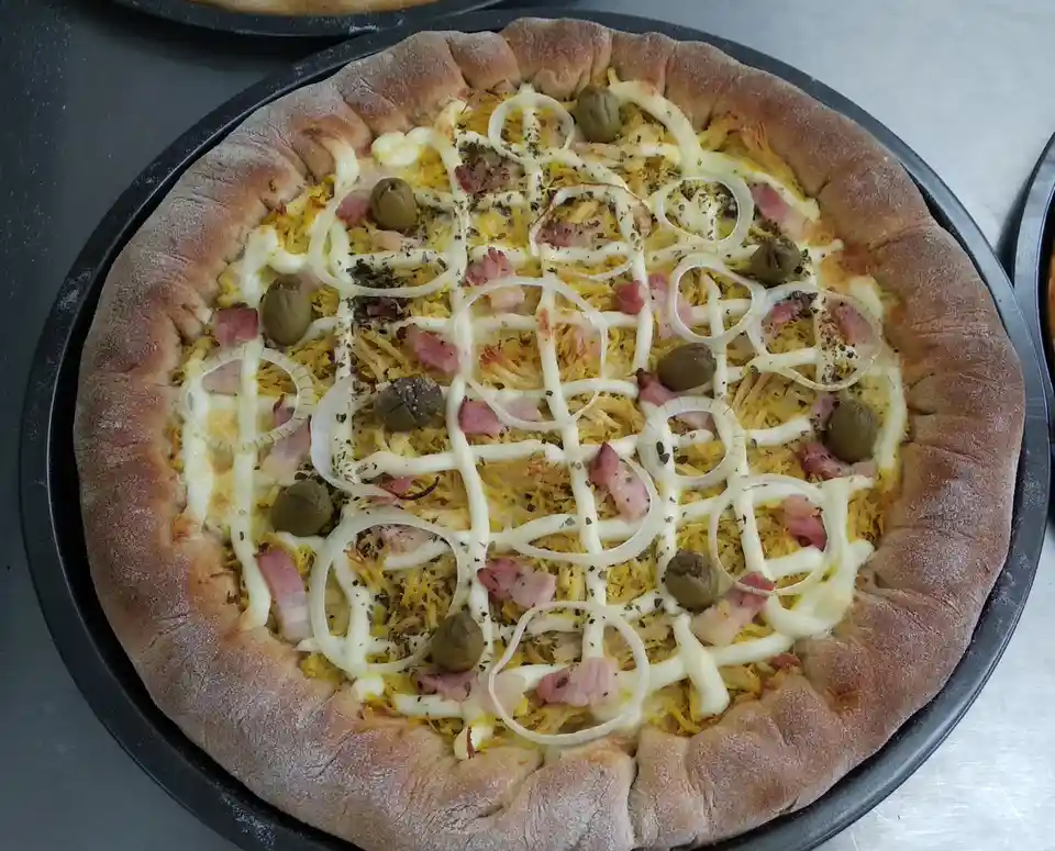 A freshly baked pizza with a thick, rustic crust sits on a black pan, topped with shredded yellow cheese, diced ham, green…
