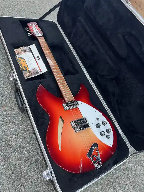 A red and orange sunburst electric guitar with a white pickguard and multiple knobs rests in an open black-lined hard case…