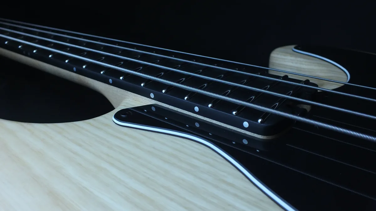 A close-up photo of a bass guitar's neck and body, showing the strings, frets, and wood grain against a dark background. The…