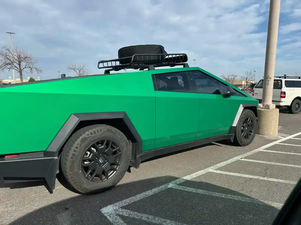 A bright green, angular, futuristic-looking electric pickup truck, resembling a Tesla Cybertruck, is parked in a lot. It has…