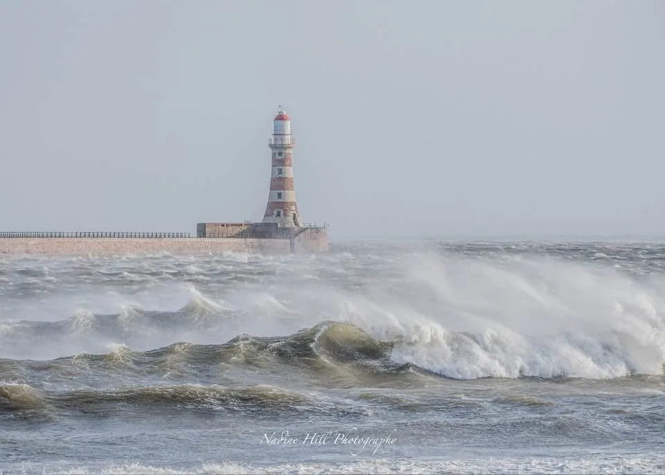 A lighthouse stands resiliently on a pier as massive, turbulent waves crash violently around its base. The overlaid text…
