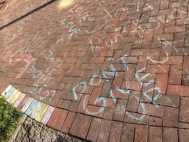 A paved brick walkway covered in faded chalk drawings and messages, including a large blue heart and the phrase 'love is…