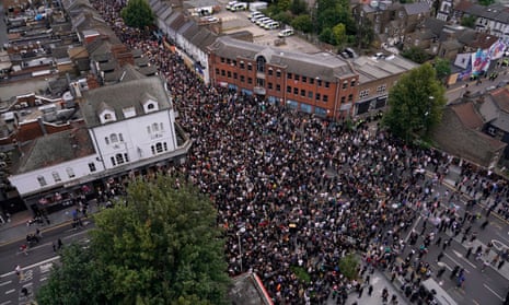 an aerial photograph shows a dense crowd of people filling a narrow town street, spilling onto sidewalks and surrounding…