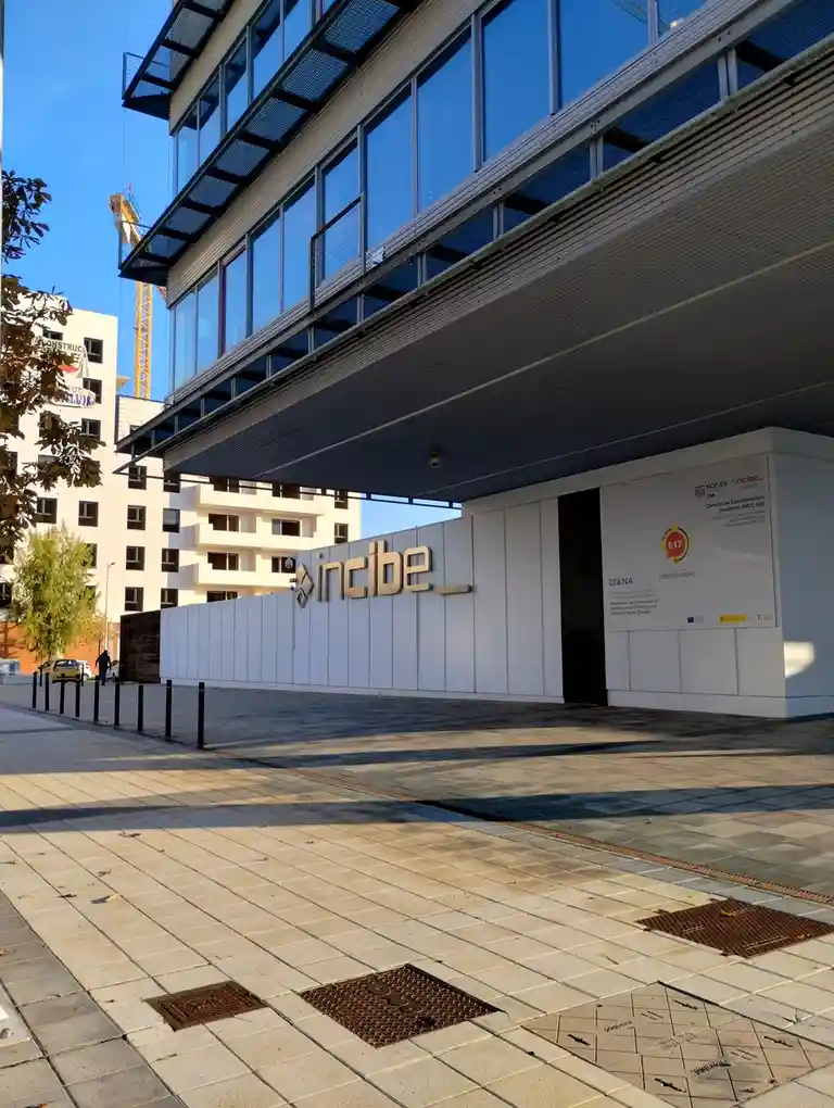 An exterior photo of a modern building with a large 'incibe' sign on a white wall, featuring glass windows and a paved…