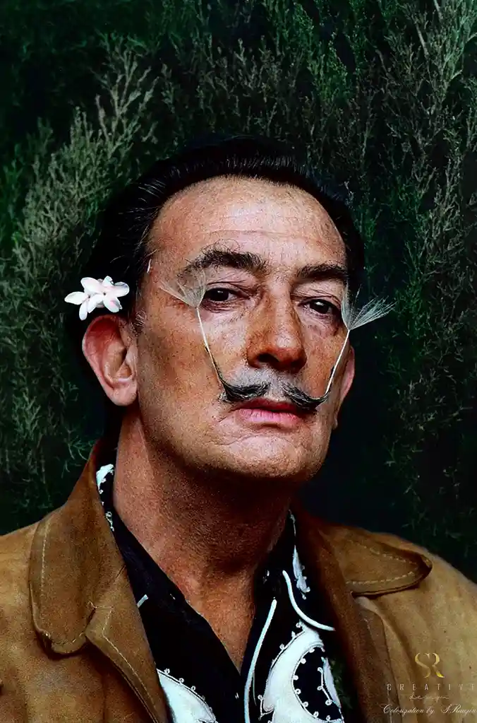 A colorized portrait of Salvador Dalí shows him with a dandelion seed head attached to each eye and a flower in his ear…