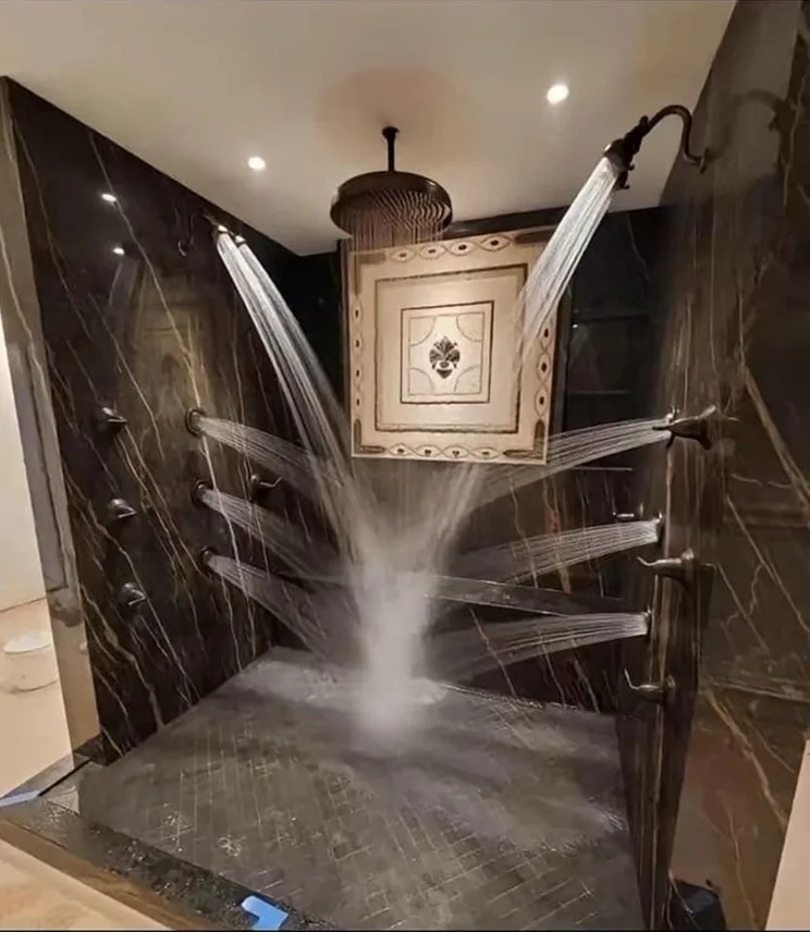 a luxurious, high-end shower stall with dark marble walls and floor, featuring multiple powerful water jets spraying from…
