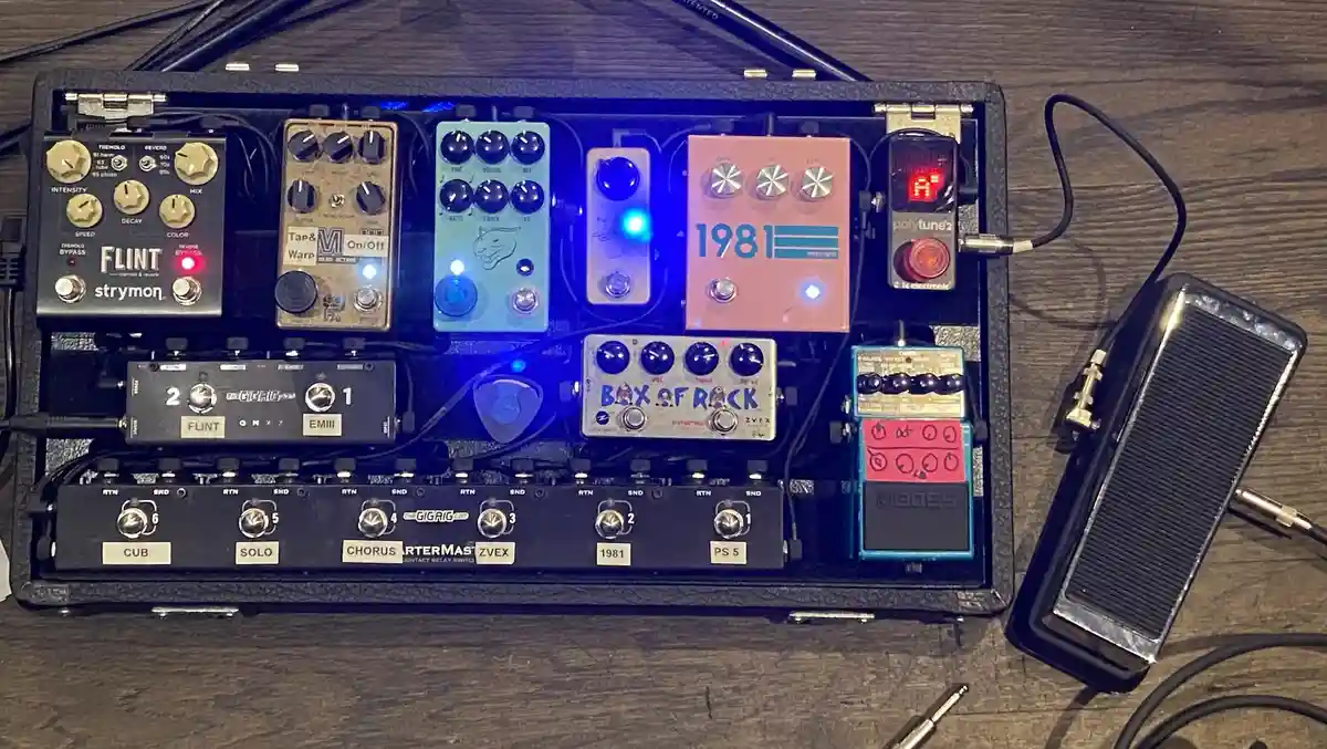 An overhead shot of a densely packed guitar pedalboard filled with various effects pedals, including a pink '1981' pedal, a…
