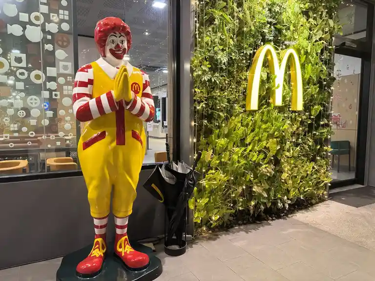 A life-sized Ronald McDonald statue stands with hands clasped in a prayer-like gesture, positioned outside a McDonald's…