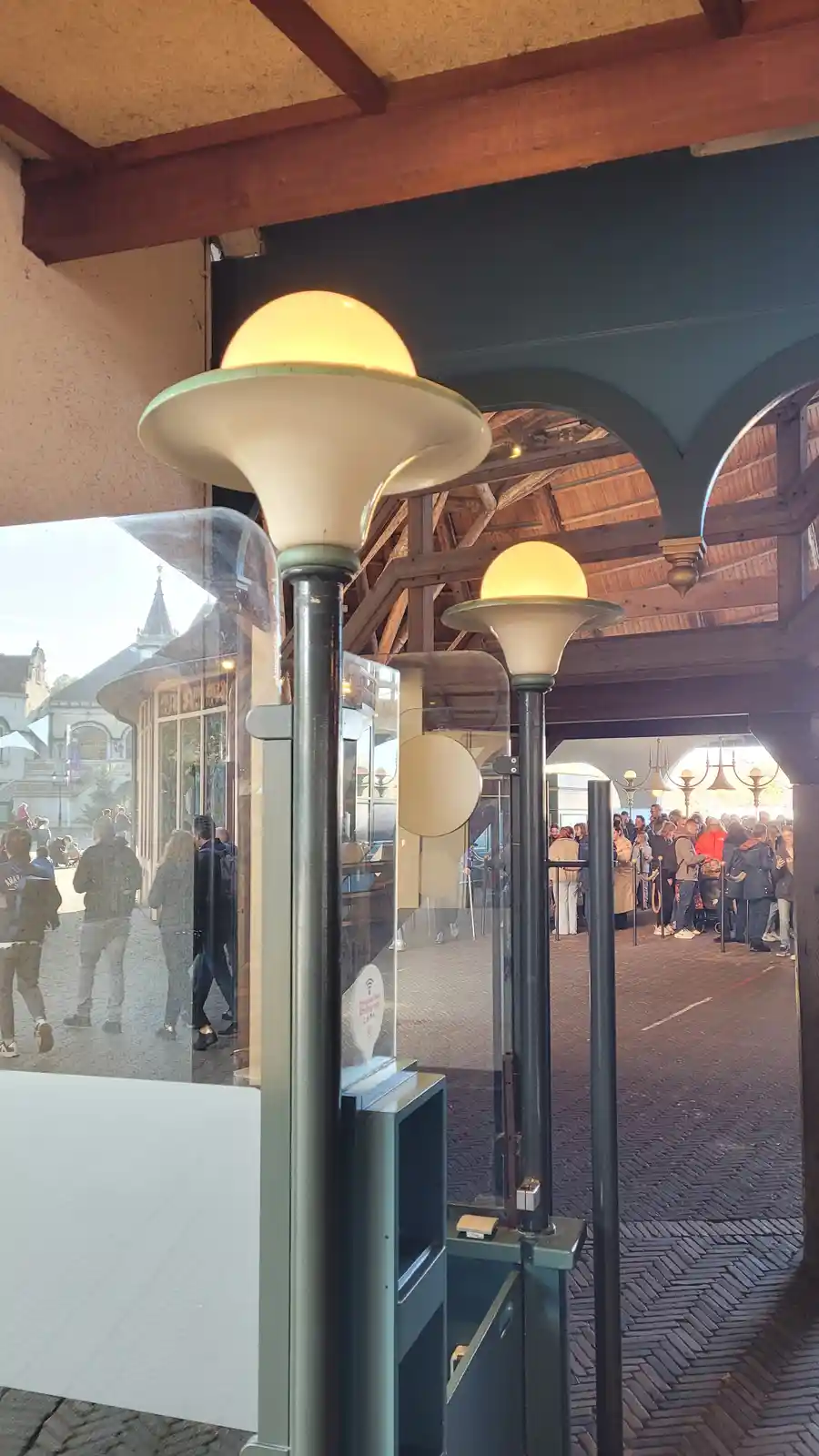 A photo shows two vintage-style street lamps with glowing bulbs in front of a glass barrier, with crowds of people visible…