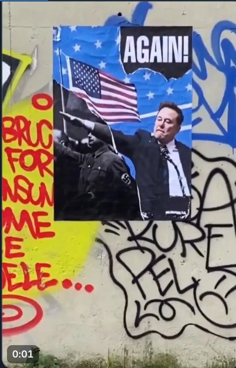 A poster taped to a graffiti-covered wall shows a photo of Elon Musk and a black-and-white image of Adolf Hitler both…