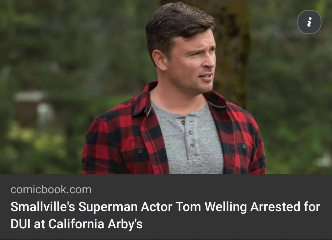 A man with short brown hair wearing a red and black plaid shirt over a grey henley shirt looks off to the side with a…
