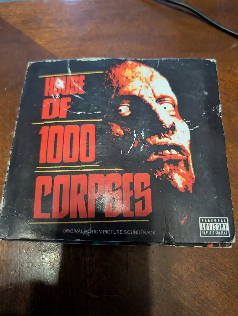 A heavily worn and scratched soundtrack cover for the movie 'House of 1000 Corpses' featuring a grotesque, blood-splattered…