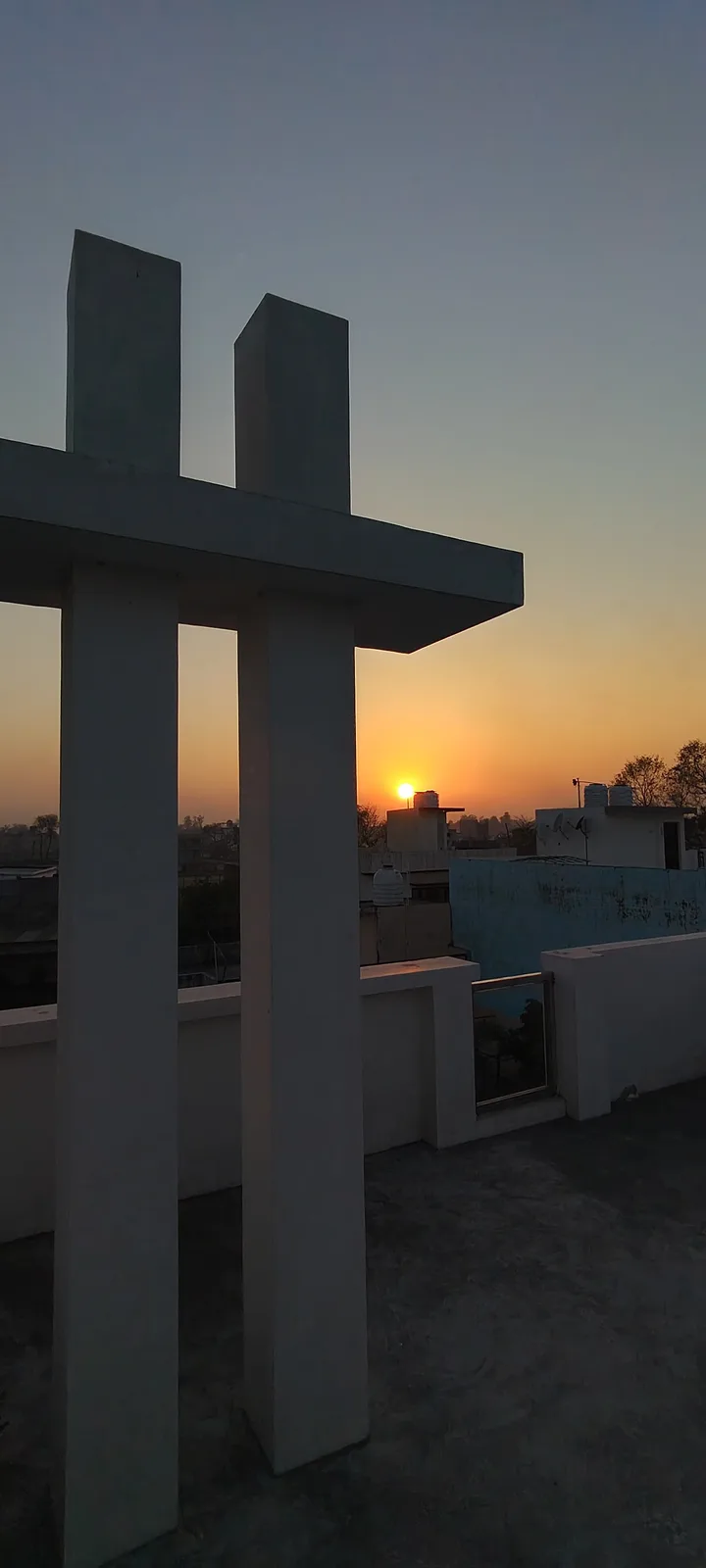 A rooftop photo at sunrise shows a concrete structure resembling a cross, with the sun rising behind it. The sky transitions…